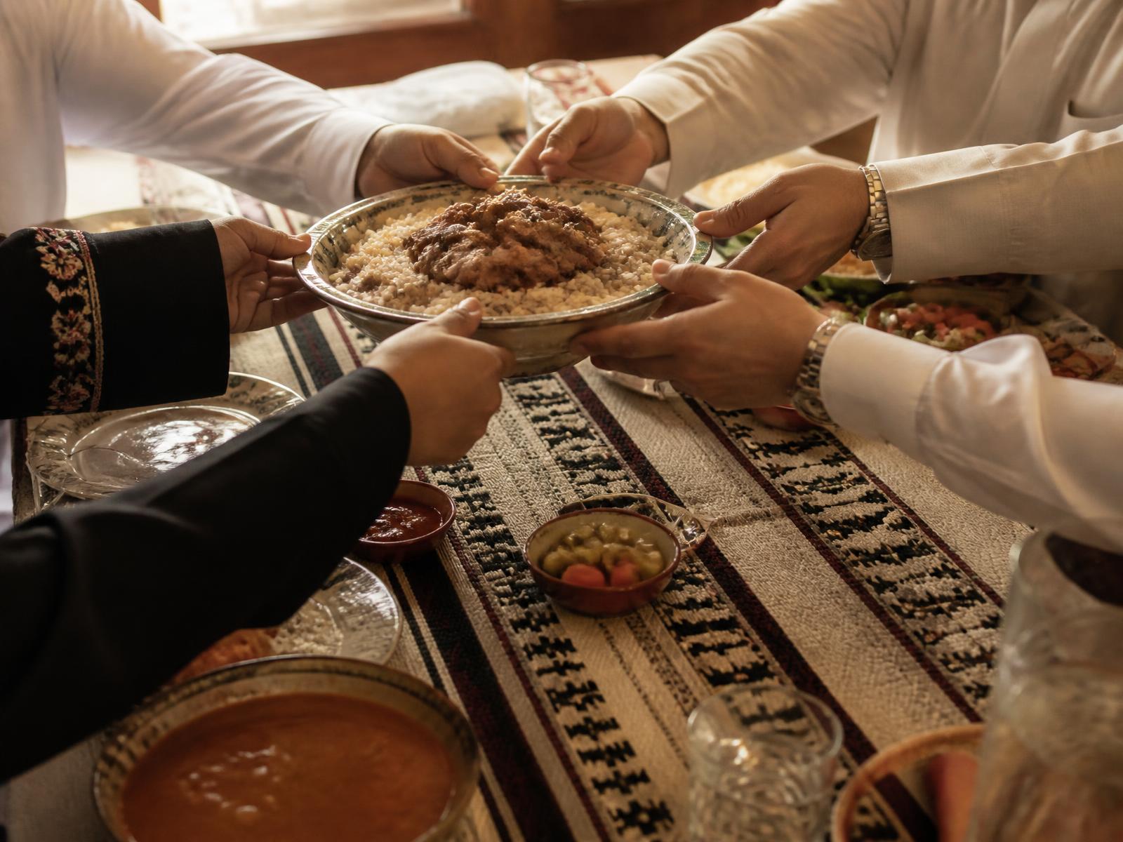 أيادٍ تتشارك تمرير طبق أرز فوق سفرة عليها نسيج سدو